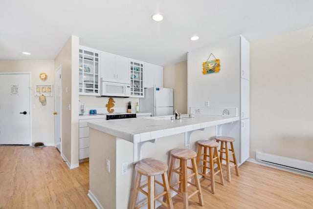 kitchen with a breakfast bar, white appliances, white cabinetry, and light hardwood / wood-style flooring