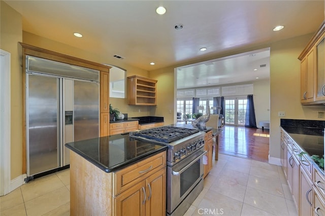 kitchen with high end appliances, a kitchen island, dark stone countertops, and light wood-type flooring