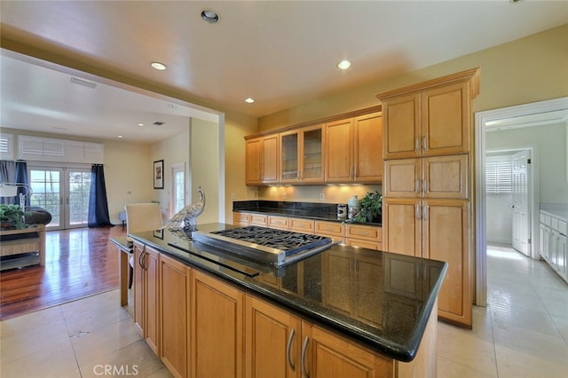 kitchen with a kitchen island, dark stone countertops, light tile floors, stainless steel gas cooktop, and backsplash