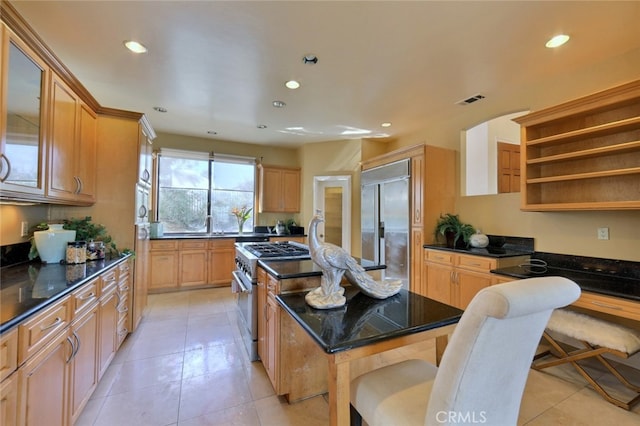 kitchen featuring light tile floors, dark stone countertops, high end appliances, a breakfast bar area, and a center island