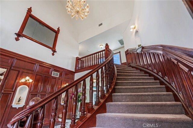 staircase with an inviting chandelier, high vaulted ceiling, and hardwood / wood-style flooring