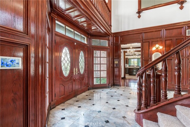 entryway featuring a chandelier, a towering ceiling, and wooden walls