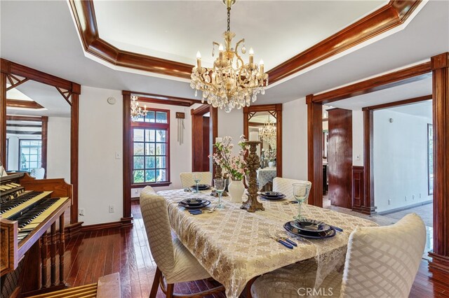 dining area with a chandelier, a raised ceiling, dark wood-type flooring, and crown molding