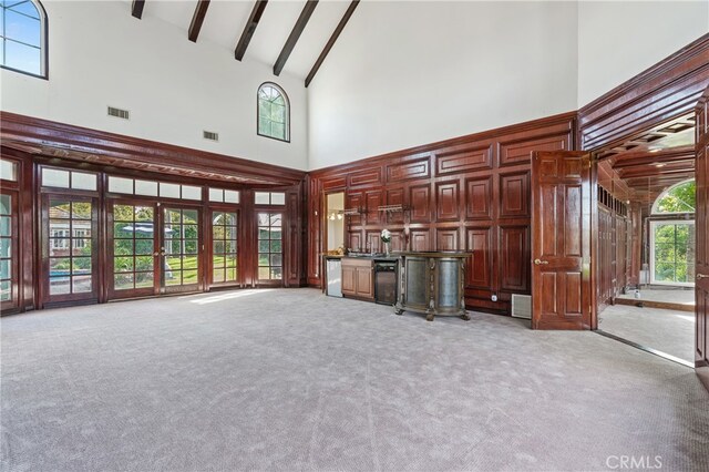 unfurnished living room with light carpet, beamed ceiling, and high vaulted ceiling