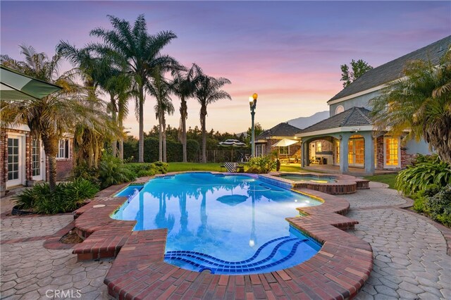 pool at dusk with a patio area and an in ground hot tub