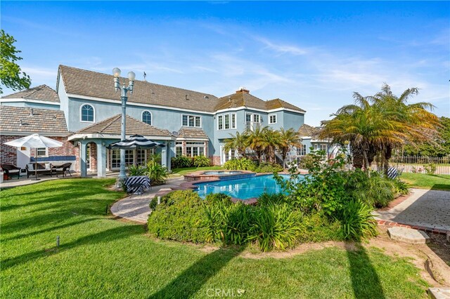 rear view of house with a swimming pool with hot tub, a yard, and a patio