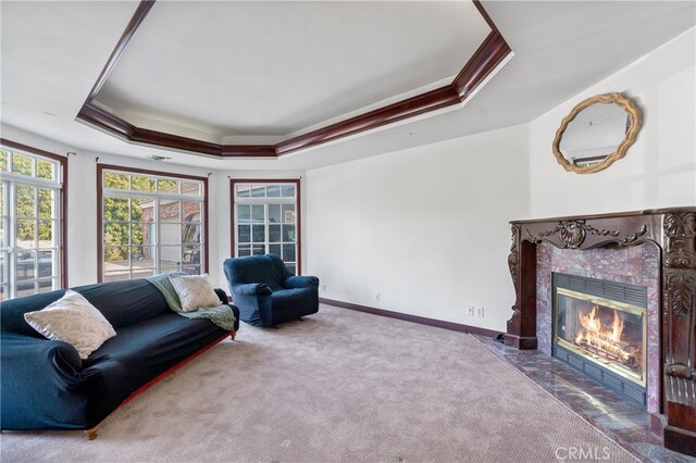 carpeted living room featuring a raised ceiling, a fireplace, and ornamental molding