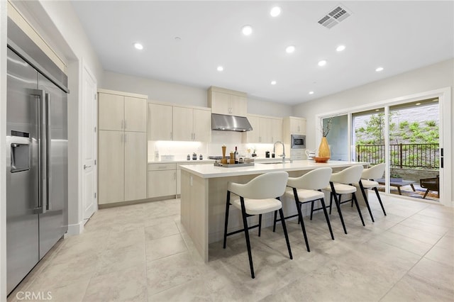 kitchen with light tile floors, a center island with sink, a breakfast bar, and built in appliances