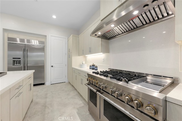 kitchen featuring high quality appliances, wall chimney exhaust hood, and white cabinetry