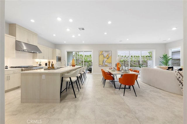 kitchen with a center island with sink, light tile floors, a kitchen breakfast bar, and a wealth of natural light