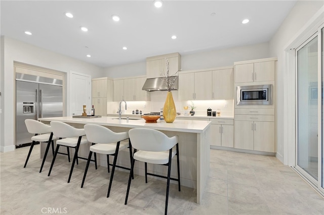 kitchen featuring built in appliances, a kitchen island with sink, sink, light tile floors, and a breakfast bar area