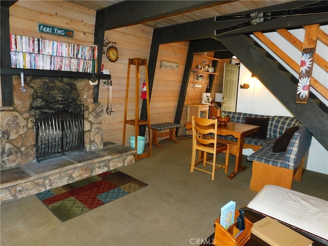 carpeted living room with wooden walls, a stone fireplace, and beamed ceiling