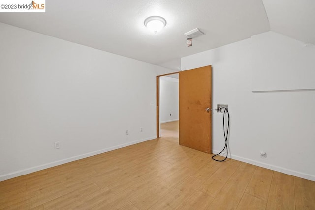 spare room with light hardwood / wood-style flooring and vaulted ceiling