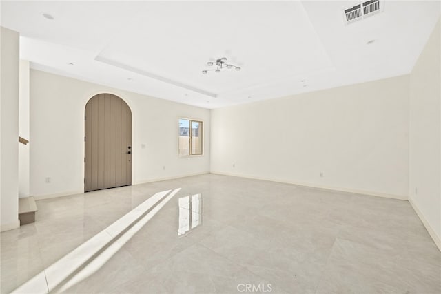 tiled empty room featuring a raised ceiling