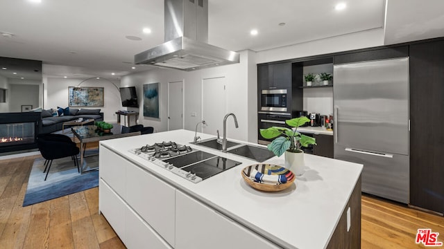 kitchen with a kitchen island with sink, light hardwood / wood-style flooring, built in appliances, island range hood, and white cabinetry