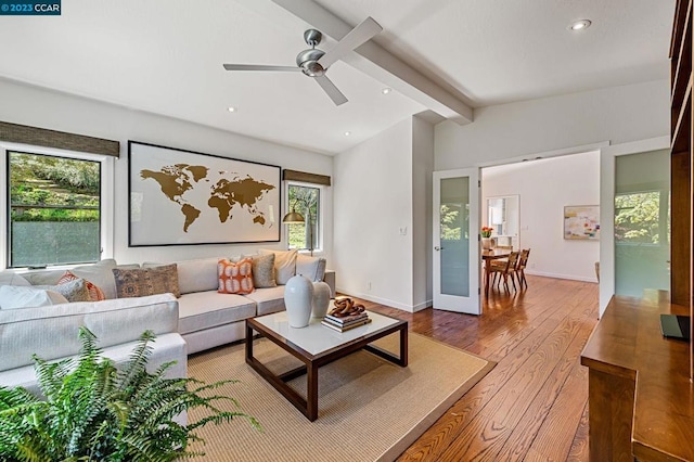 living room featuring light hardwood / wood-style floors, ceiling fan, a wealth of natural light, and beamed ceiling