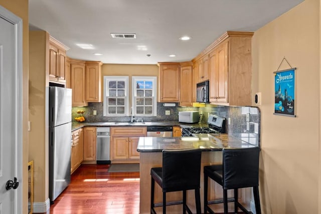 kitchen with tasteful backsplash, a kitchen breakfast bar, appliances with stainless steel finishes, dark wood-type flooring, and kitchen peninsula