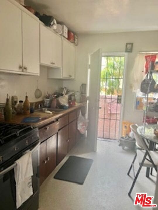 kitchen featuring stainless steel gas stove, white cabinetry, and sink