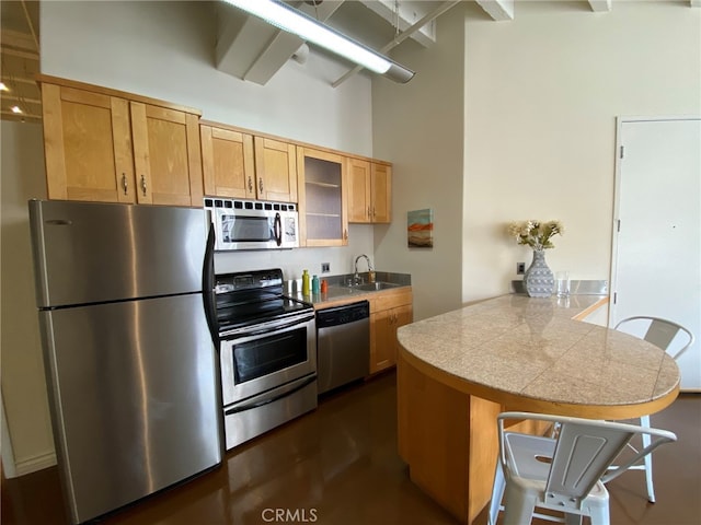 kitchen with appliances with stainless steel finishes, kitchen peninsula, a breakfast bar area, a high ceiling, and sink