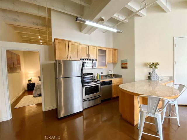 kitchen with appliances with stainless steel finishes, a kitchen breakfast bar, kitchen peninsula, a high ceiling, and sink