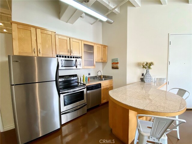 kitchen featuring appliances with stainless steel finishes, a kitchen breakfast bar, kitchen peninsula, light brown cabinetry, and sink