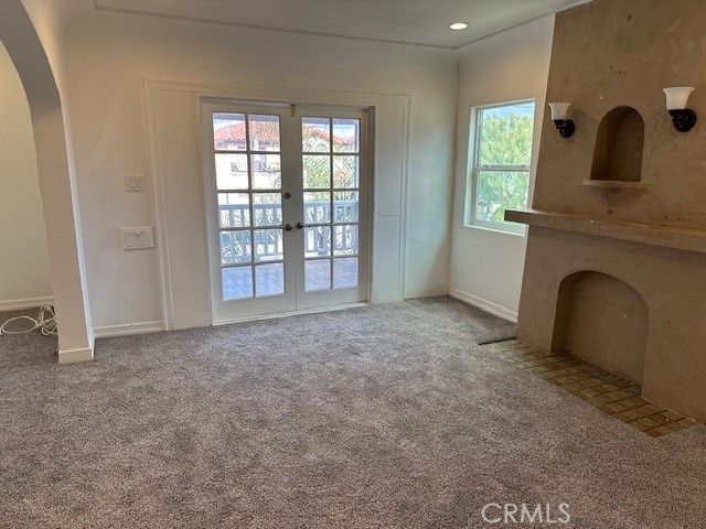 unfurnished living room featuring baseboards, arched walkways, carpet flooring, and french doors