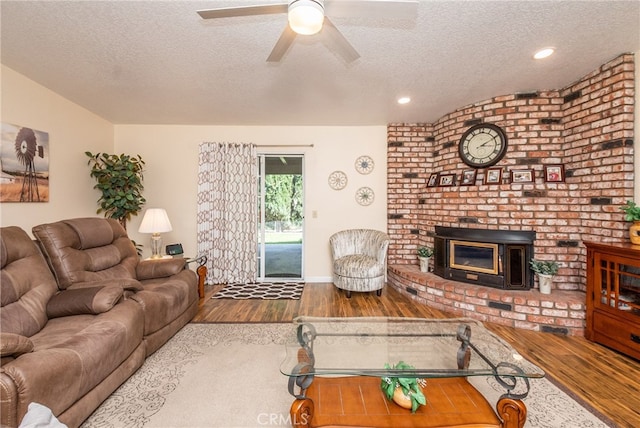 living room featuring a textured ceiling, wood-type flooring, a wood stove, and ceiling fan