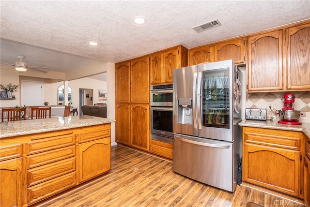 kitchen featuring backsplash, stainless steel appliances, a textured ceiling, and light hardwood / wood-style flooring