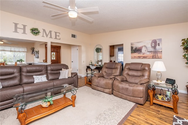 living room featuring light hardwood / wood-style floors, a textured ceiling, and ceiling fan