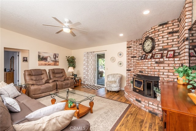 living room with hardwood / wood-style floors, ceiling fan, a textured ceiling, vaulted ceiling, and a wood stove