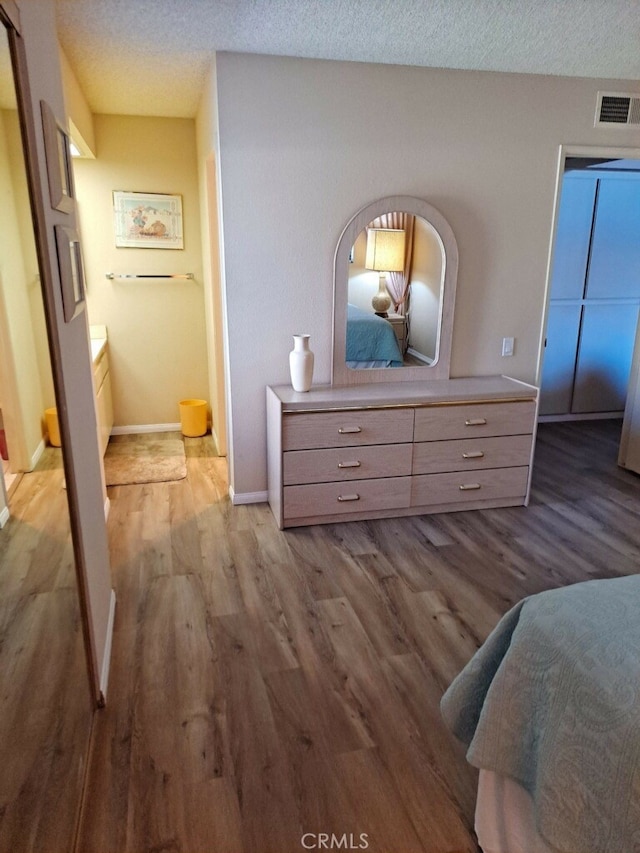 bedroom with connected bathroom, light hardwood / wood-style flooring, and a textured ceiling