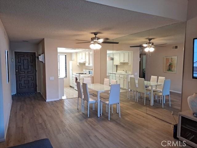 dining space with ceiling fan, light wood-type flooring, sink, and a textured ceiling