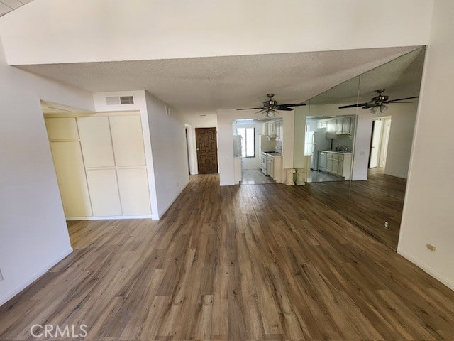 unfurnished living room featuring ceiling fan, dark wood-type flooring, and a textured ceiling