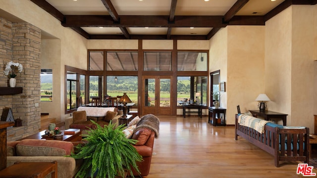 living room with a stone fireplace, light hardwood / wood-style floors, beam ceiling, and a towering ceiling