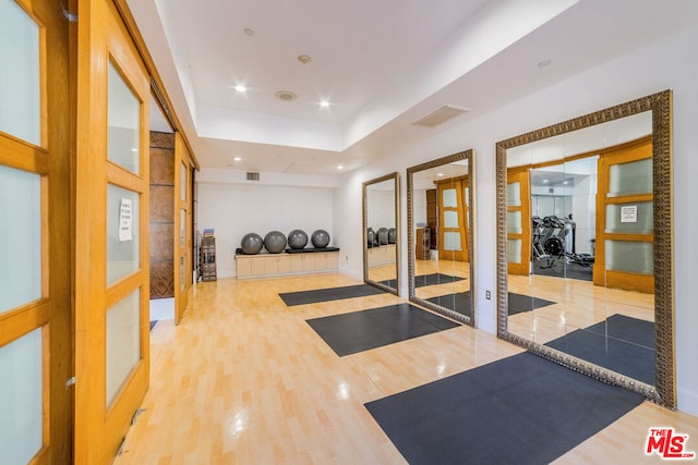 exercise area with wood-type flooring, a tray ceiling, and basketball hoop