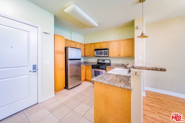 kitchen featuring kitchen peninsula, light wood-type flooring, stainless steel appliances, sink, and decorative light fixtures