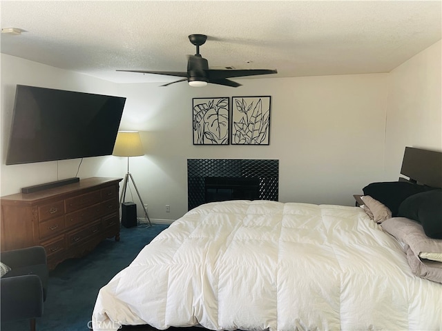 bedroom featuring ceiling fan, a textured ceiling, dark carpet, and a tile fireplace