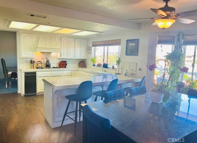 kitchen with dark hardwood / wood-style flooring, a breakfast bar, kitchen peninsula, white cabinets, and premium range hood