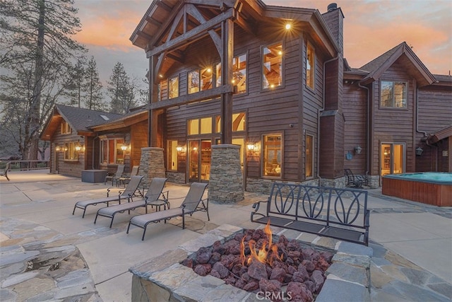 42143 Switzerland Dr, Big Bear, CA 92315 - back of house at dusk featuring a hot tub, a patio area, an outdoor fire pit, and a chimney
