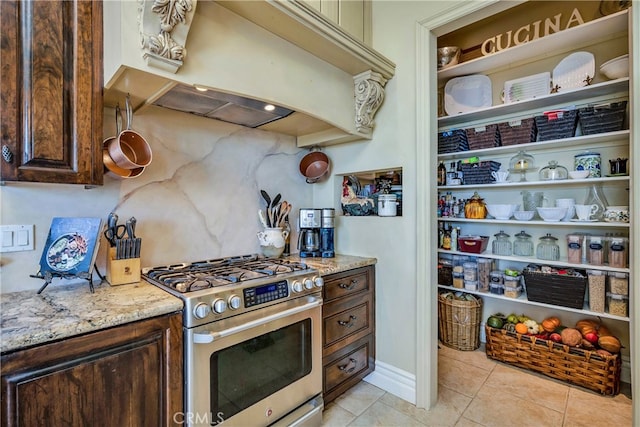 kitchen featuring custom exhaust hood, light tile patterned flooring, dark brown cabinets, high end stove, and light stone countertops