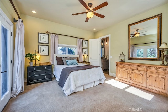 bedroom with ceiling fan, ensuite bath, and light colored carpet