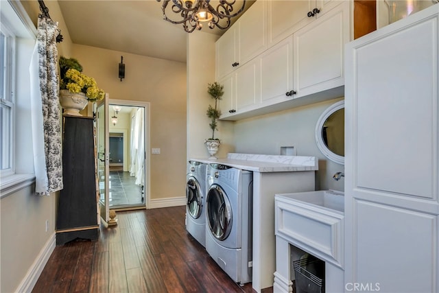 clothes washing area with a notable chandelier, washing machine and clothes dryer, dark hardwood / wood-style floors, and cabinets