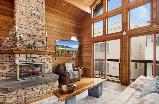 living room featuring a stone fireplace, wood walls, wood ceiling, light hardwood / wood-style flooring, and beam ceiling