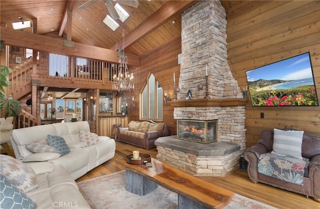 living room with light hardwood / wood-style flooring, a stone fireplace, high vaulted ceiling, and ceiling fan with notable chandelier