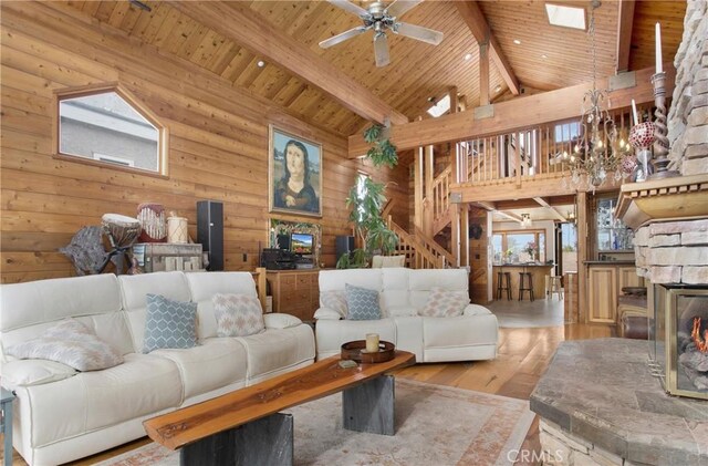 living room featuring light wood-type flooring, ceiling fan, beam ceiling, a stone fireplace, and wood ceiling