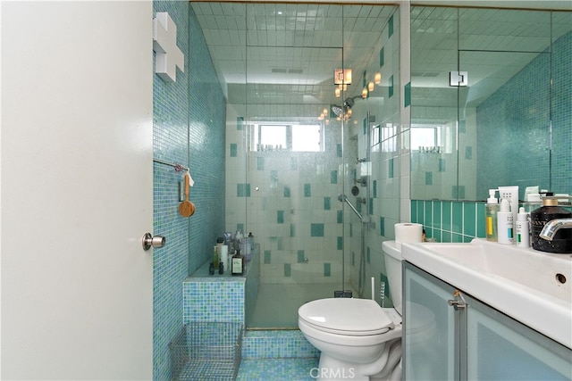 bathroom with tile walls, a shower with shower door, vanity, tile patterned flooring, and toilet