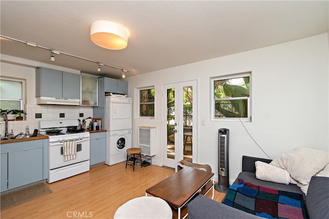 kitchen featuring light hardwood / wood-style floors, stacked washer / dryer, a textured ceiling, decorative backsplash, and white range with gas cooktop