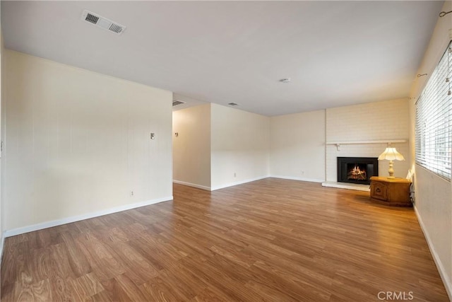 unfurnished living room with wood-type flooring and a brick fireplace