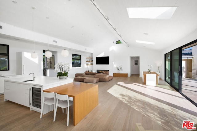 kitchen with white cabinetry, beverage cooler, pendant lighting, vaulted ceiling, and a center island with sink