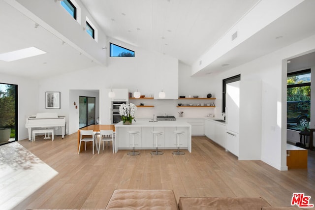 kitchen featuring white cabinetry, a kitchen breakfast bar, high vaulted ceiling, an island with sink, and light wood-type flooring